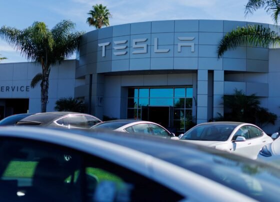 Imagem de um carro Tesla cinza, com a loja da Tesla ao fundo