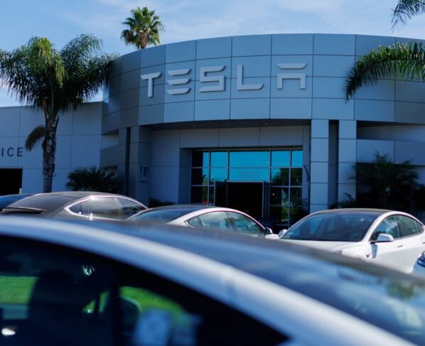 Imagem de um carro Tesla cinza, com a loja da Tesla ao fundo