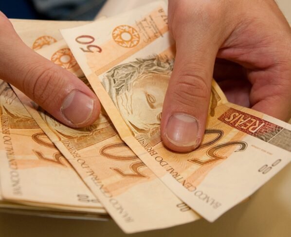 mãos segurando notas de cinquenta reais auxílio emergencial renda mínima crédito