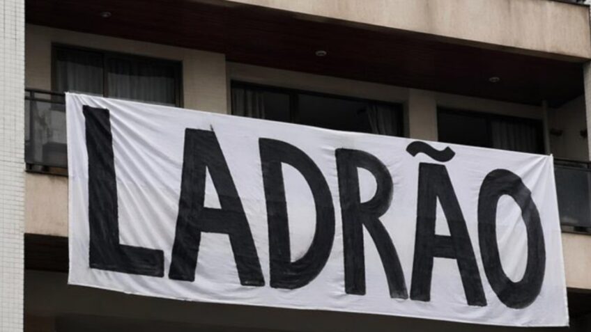 Na imagem, faixa com a palavra “ladrão” na janela do apartamento